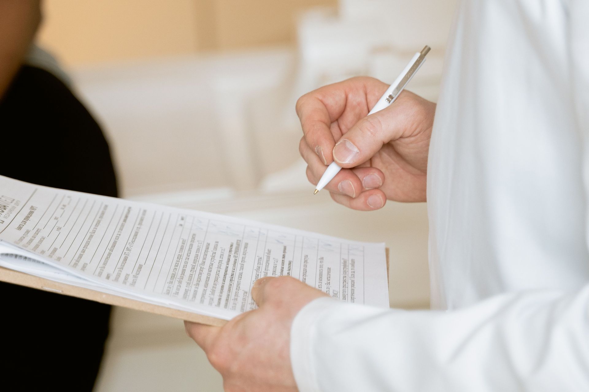 Person in white coat writing on a clipboard with a pen