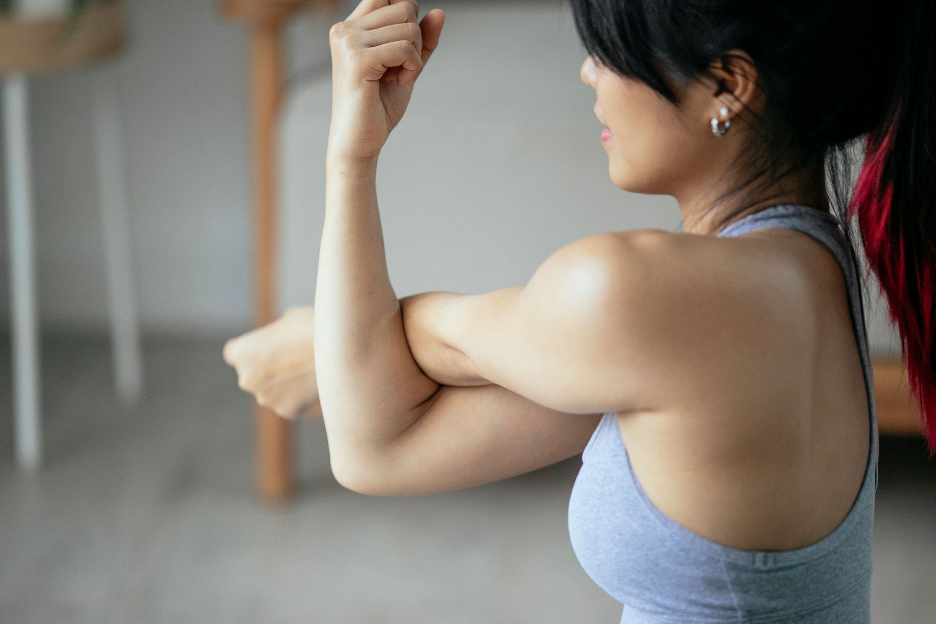 Woman in a gray sports bra flexing her arm in a bright indoor room