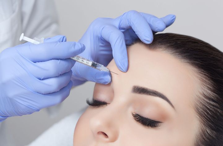 Cosmetic injection being administered to the forehead with gloved hands
