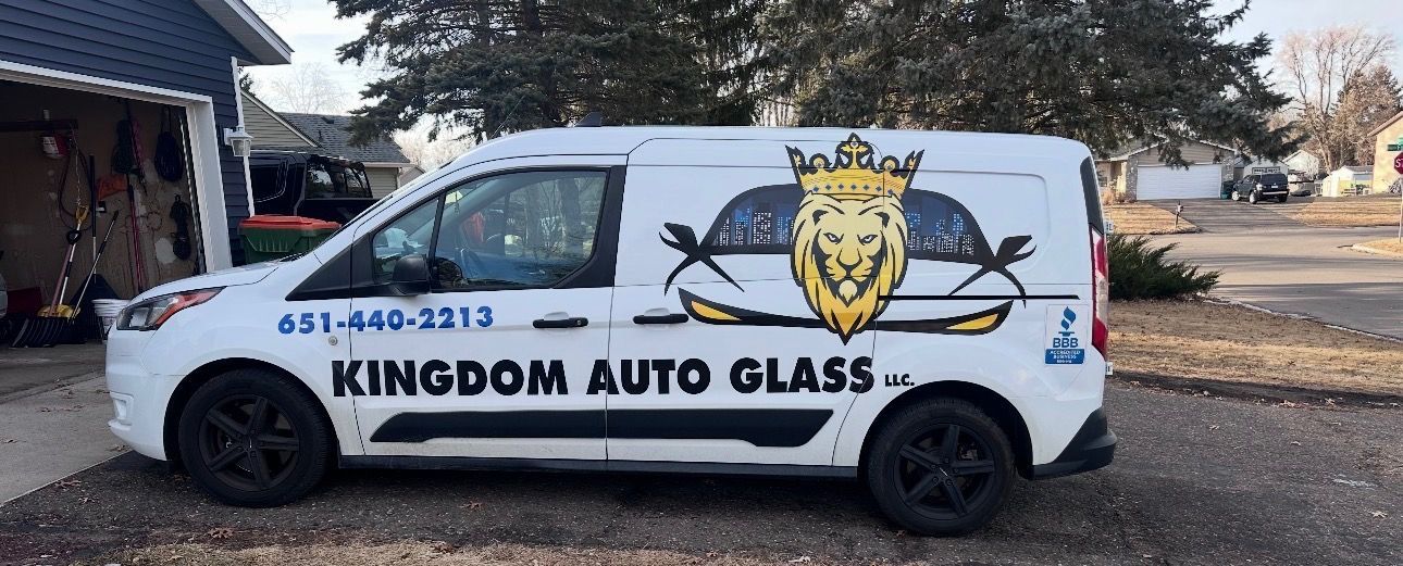 White Kingdom Auto Glass van with lion logo and phone number parked outdoors.