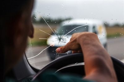 Driver’s hand on steering wheel near a cracked windshield, viewed from inside a car