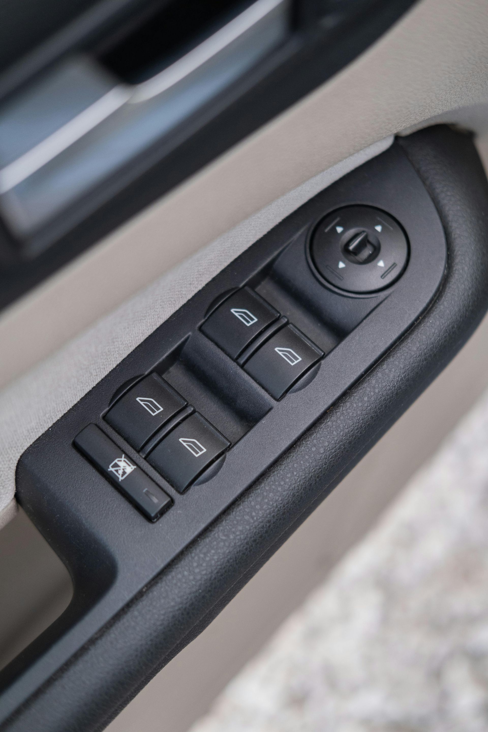 Close-up of car door window and mirror control switches on a black panel.