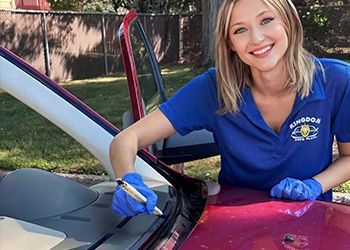 Woman in blue shirt cleaning a car windshield with a cloth outdoors