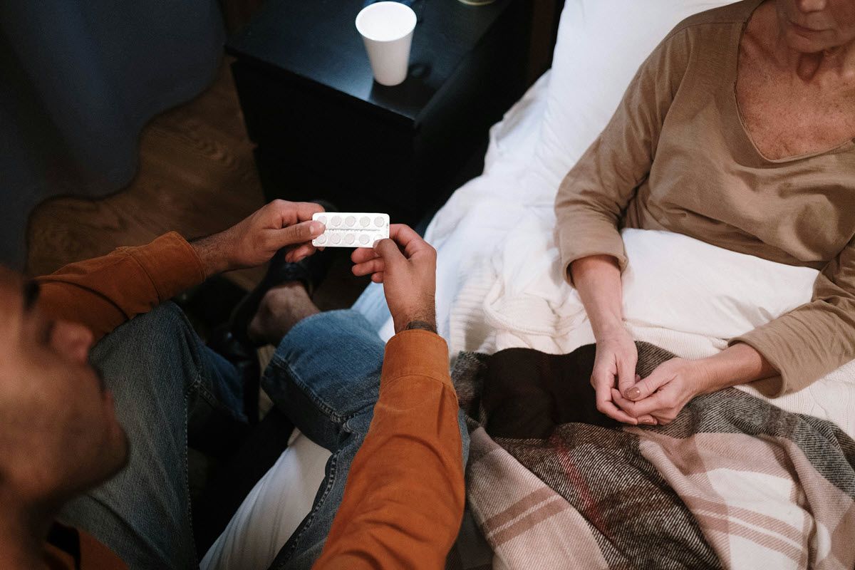 Person offering medication to someone sitting in bed.