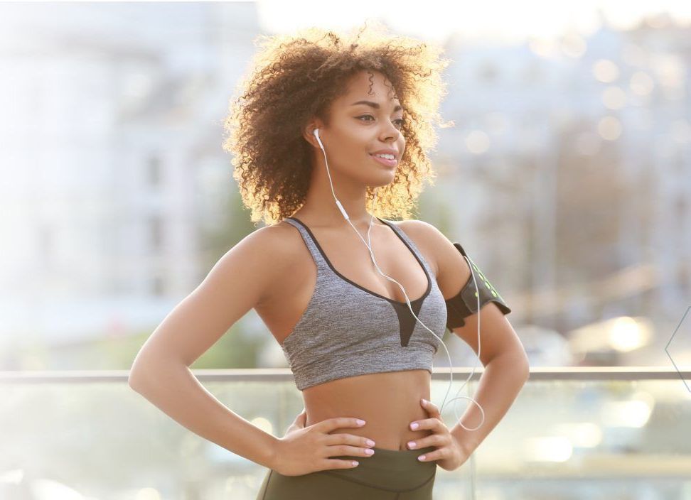 a woman wearing headphones and a sports bra is standing with her hands on her hips .