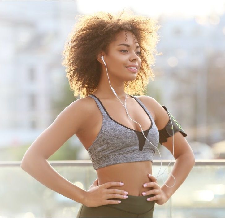 a woman wearing a sports bra and headphones stands with her hands on her hips
