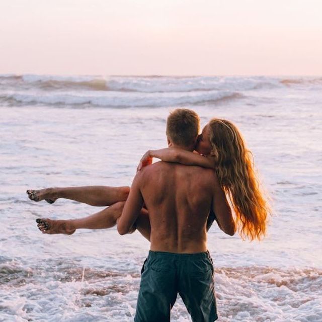 A man is carrying a woman in his arms on the beach.
