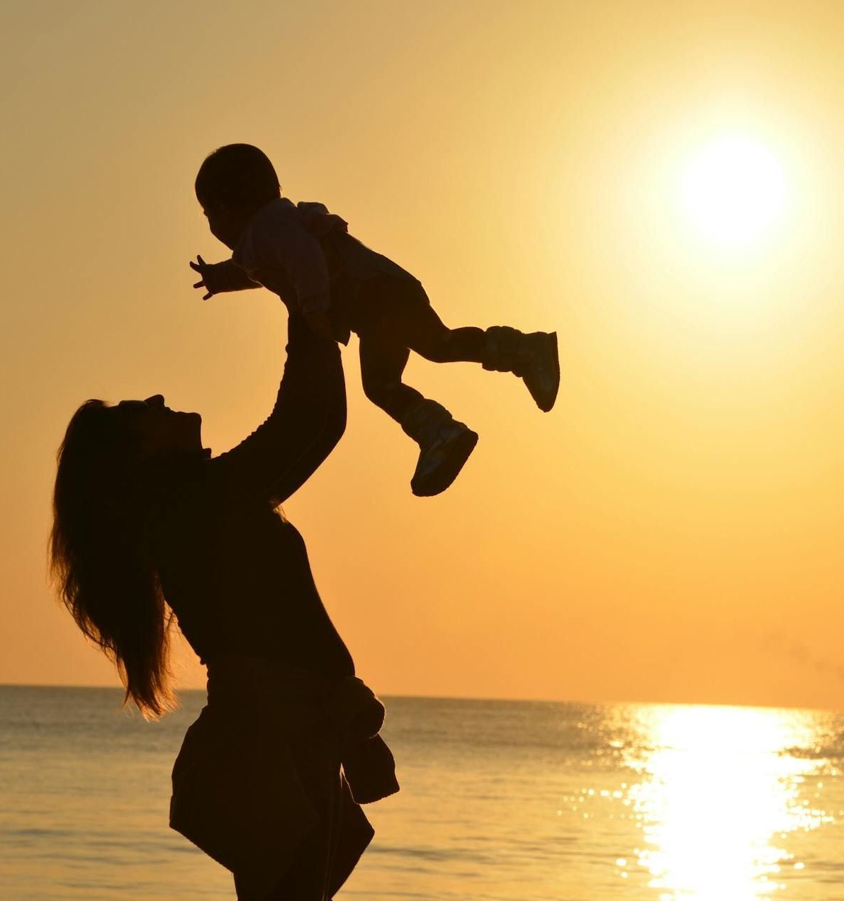 A silhouette of a woman holding a baby in the air