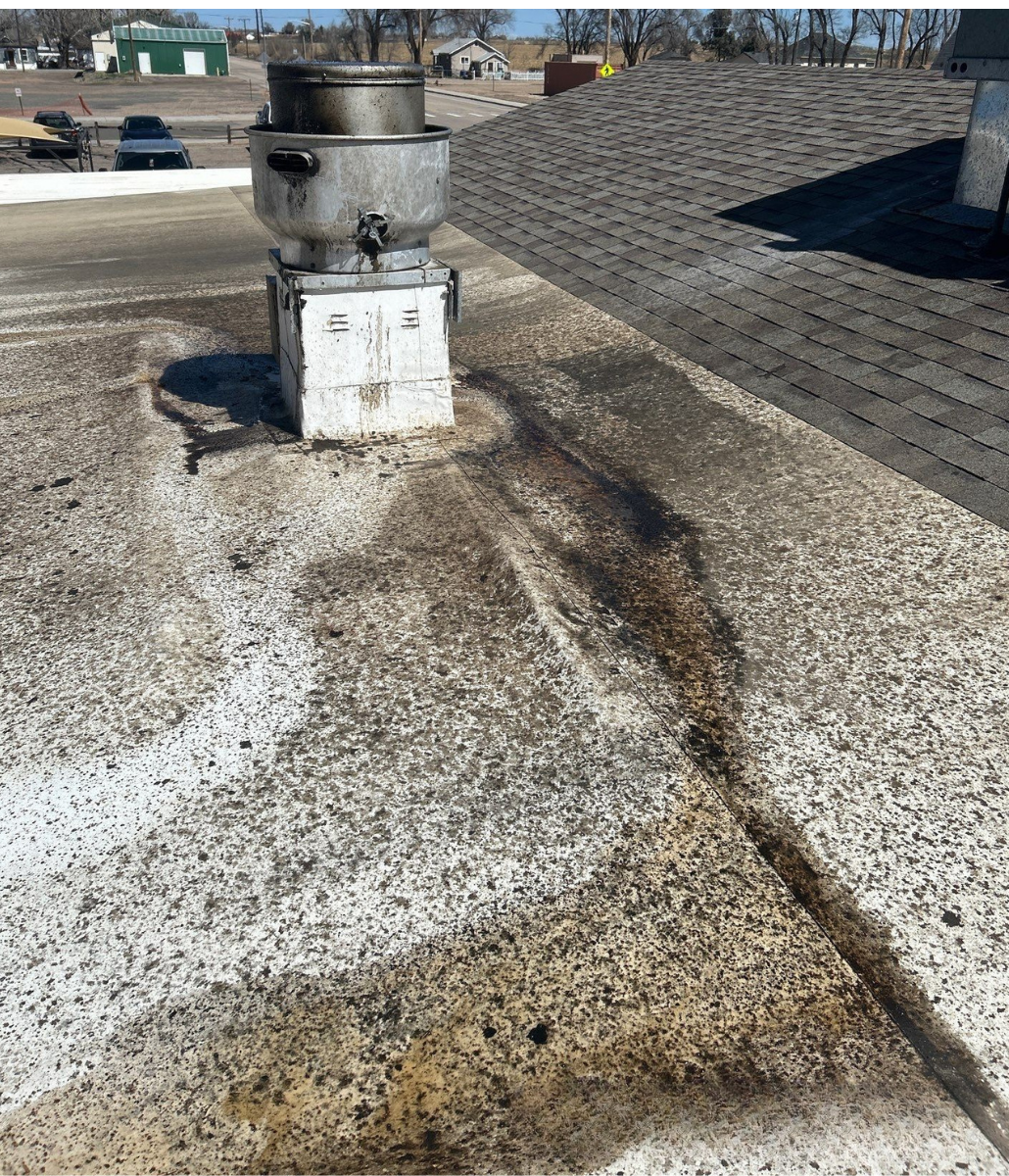 Flat roof with a vent, showing a dark stain likely from a leak. Patches of white material are scattered across the surface.