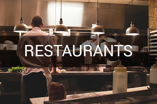 A man in an apron is standing in a restaurant kitchen.