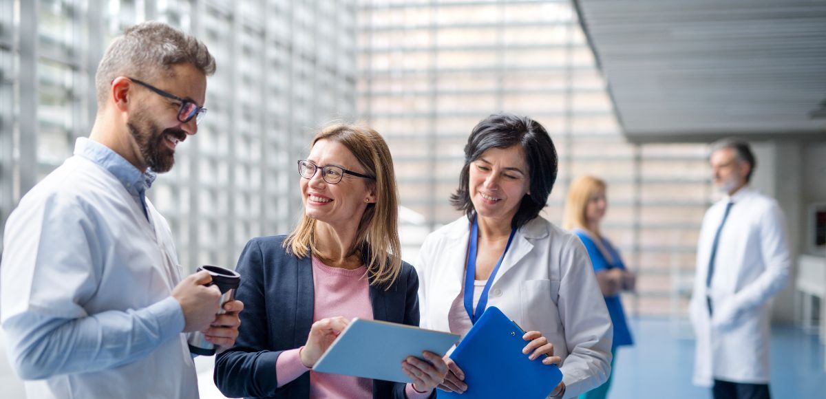 Providers and Corporate talking in a bright office hallway, one holding a blue folder.