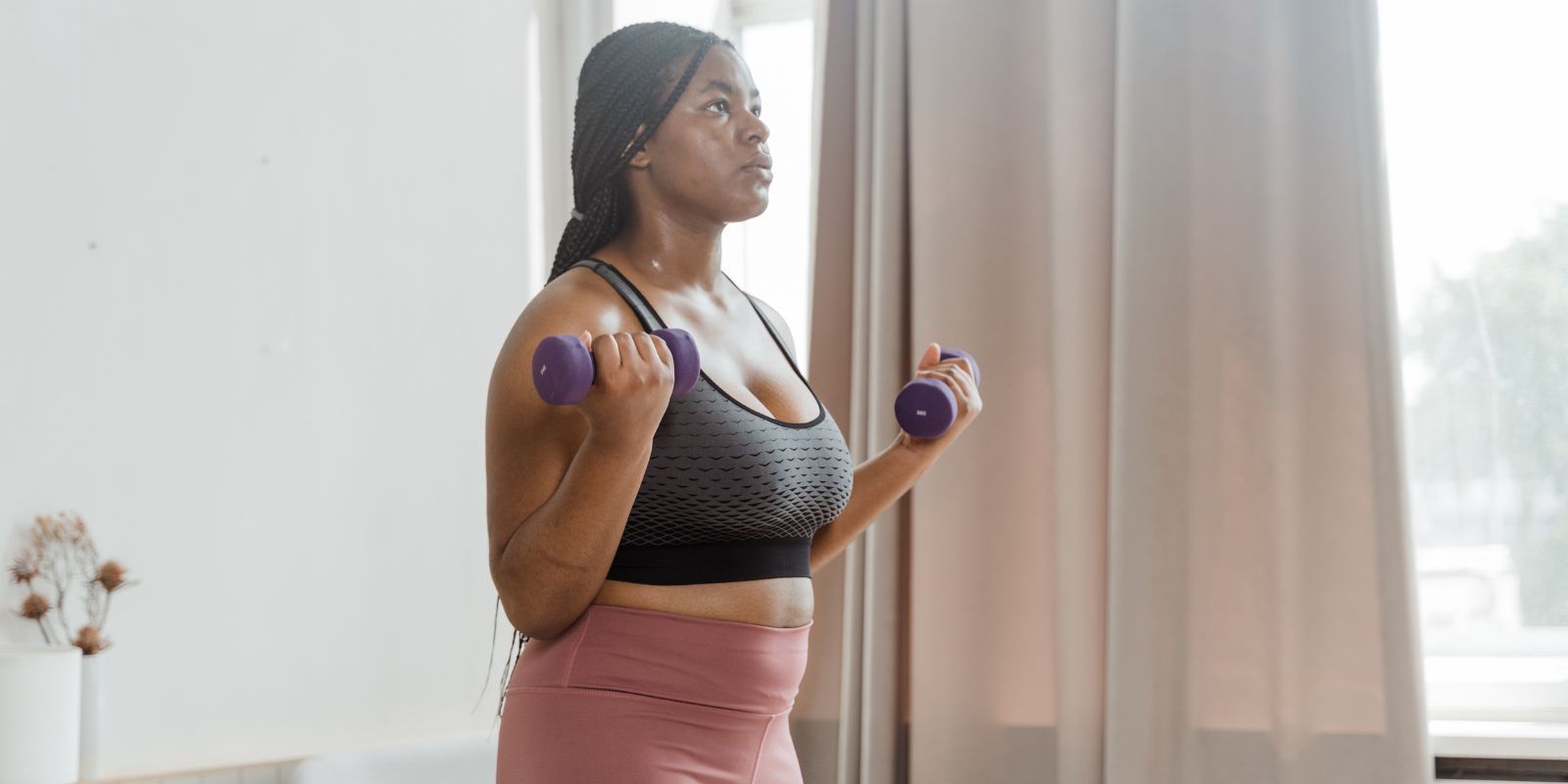 Woman exercising with dumbbells beside a window in a bright room