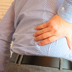 a man in a blue shirt is holding his back in pain with Radiculopathy