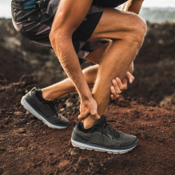 a man is kneeling down and holding his ankle in pain with Tendonitis