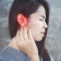a woman is holding her ear in pain from ear infection