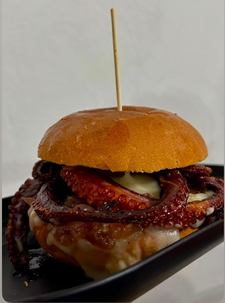 Hamburger gourmet su un piatto nero con salsa lucida e uno spiedino che trafigge il panino.