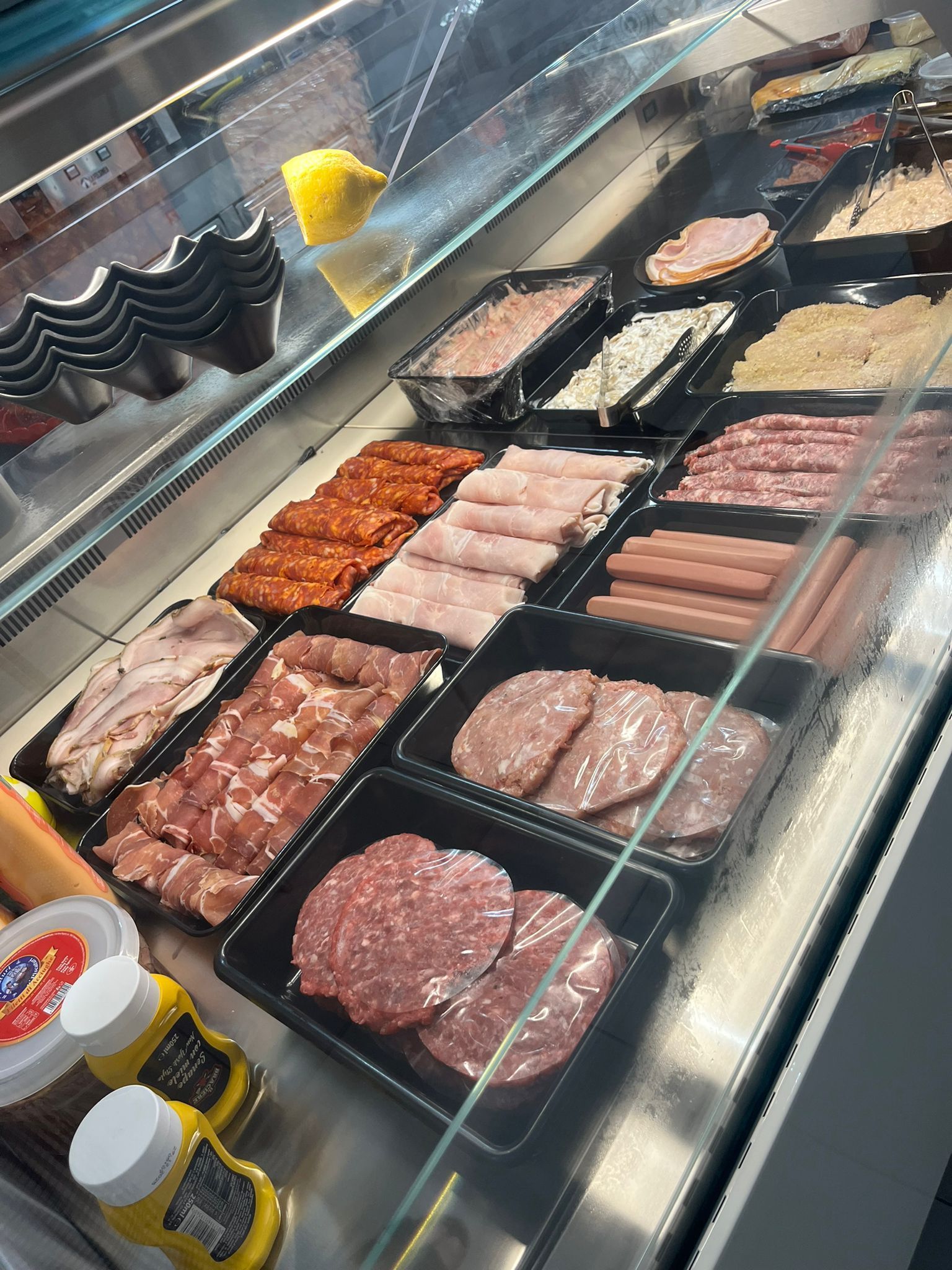 Carni crude confezionate in una vetrina refrigerata da gastronomia con bottiglie di salsa davanti.