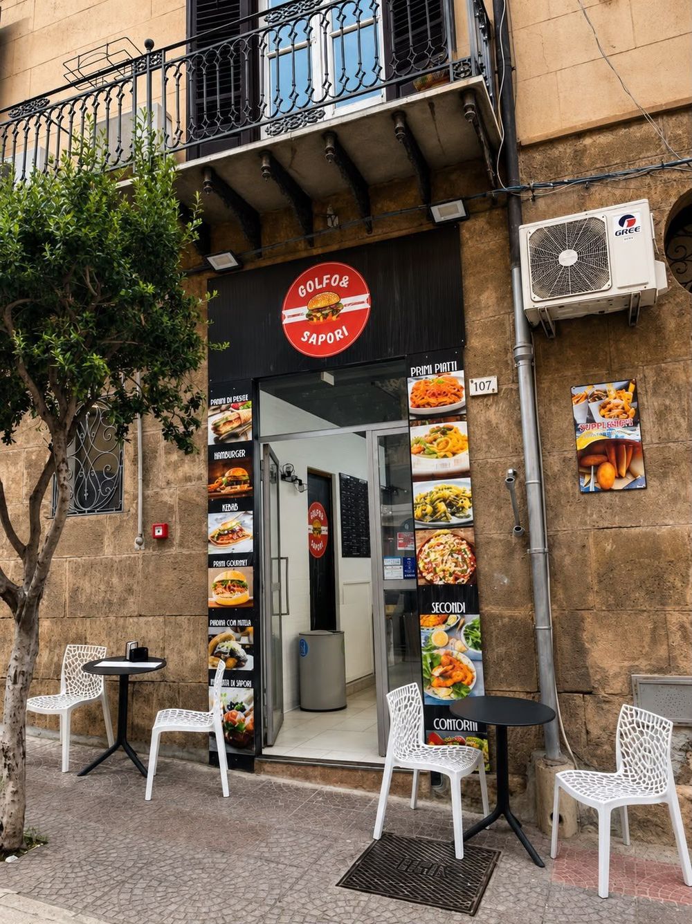 Piccolo ingresso di un caffè con tavolini e sedie all'aperto, situato su una strada stretta.