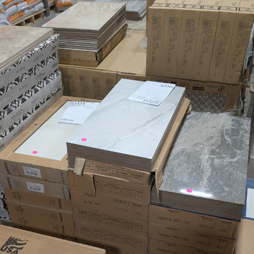 Boxes of ceramic tiles in a warehouse, varying colors, stacked, with labels.