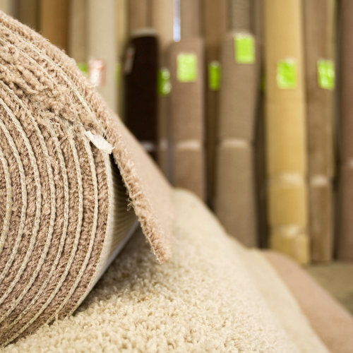 Rolls of beige and tan carpet stacked in a carpet store.