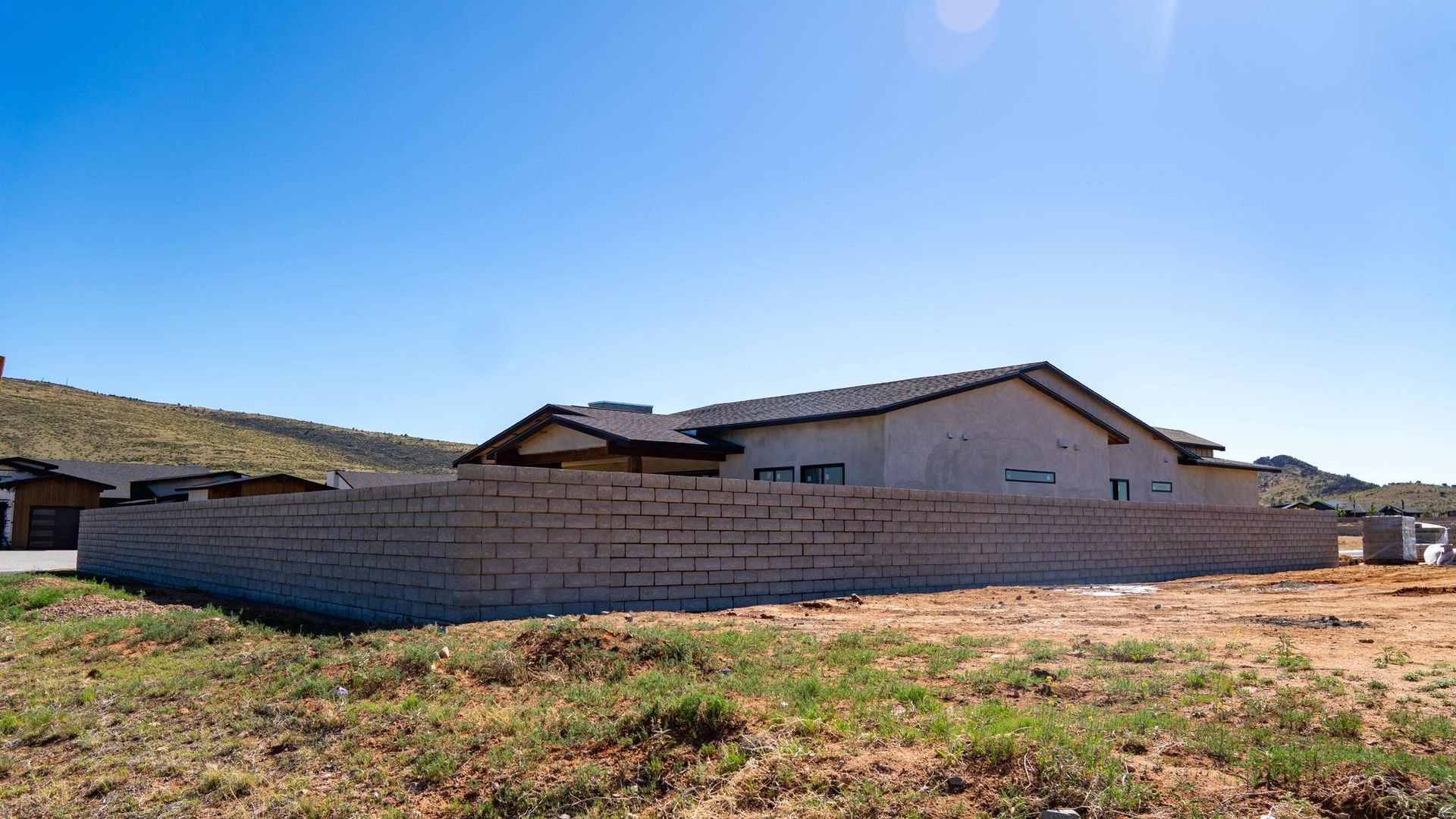A beige brick wall surrounds a modern house under a bright blue sky.