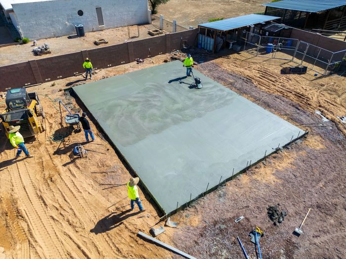 Construction crew smoothing fresh concrete slab on dirt ground outdoors.