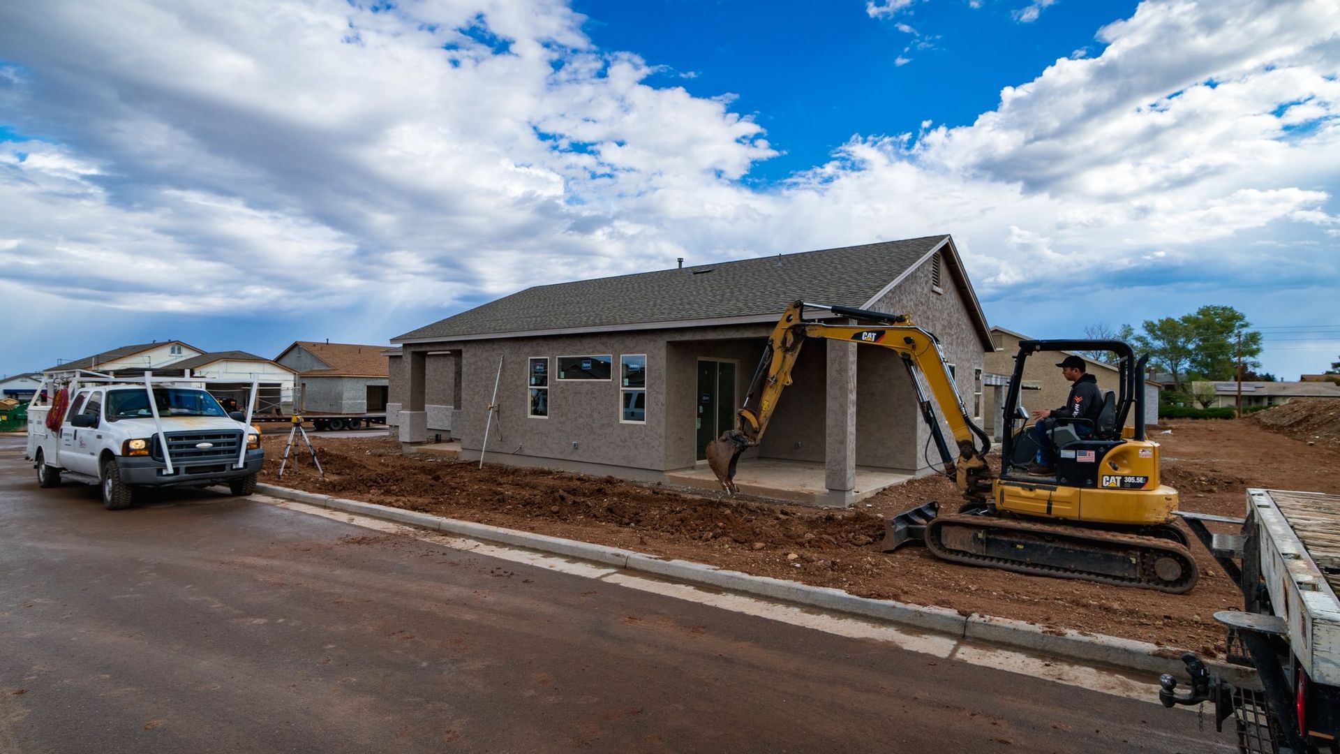 Construction workers and excavator building a brick house beside a road under a cloudy sky
