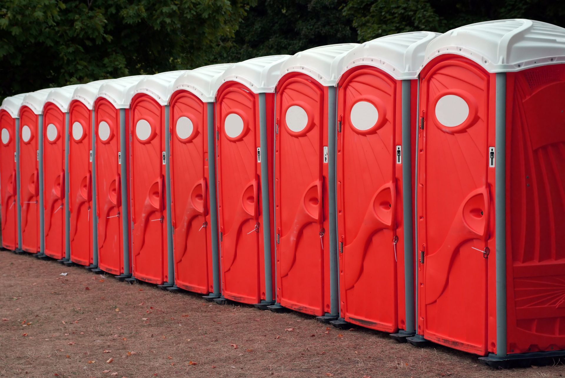 Row of red portable toilet units lined up side by side outdoors on a gravel path