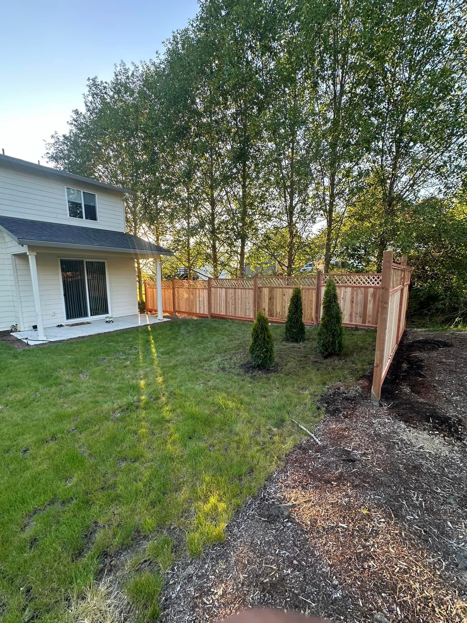 Backyard with green lawn, gravel border, trees, and a white house with a patio door