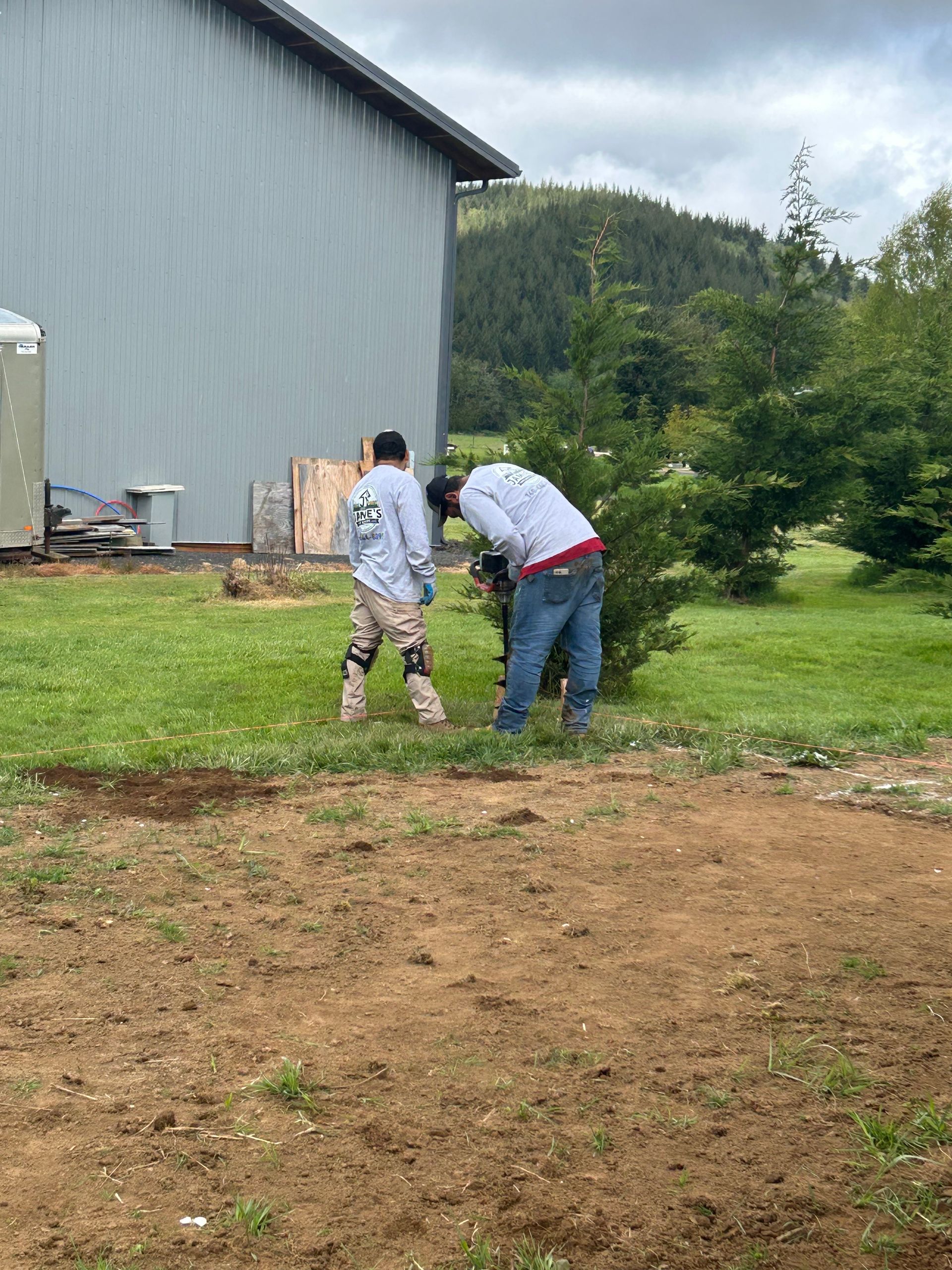 Two people bending over a garden bed near a gray building and grassy yard.
