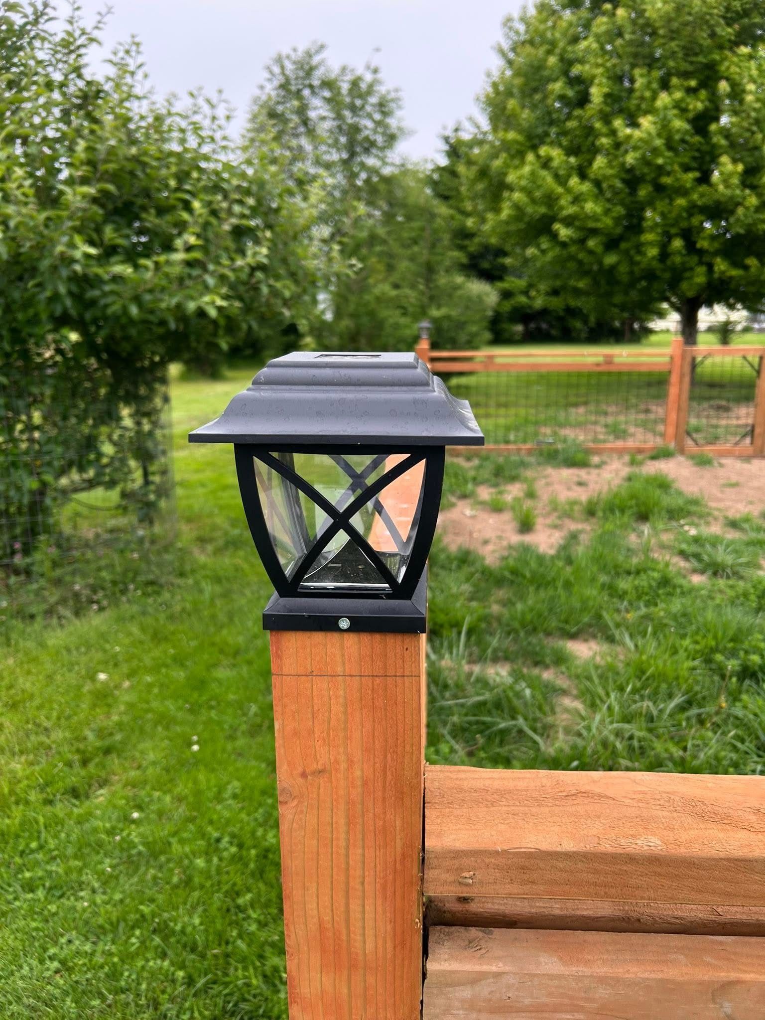 Black solar cap light on a wooden fence post in a green yard.