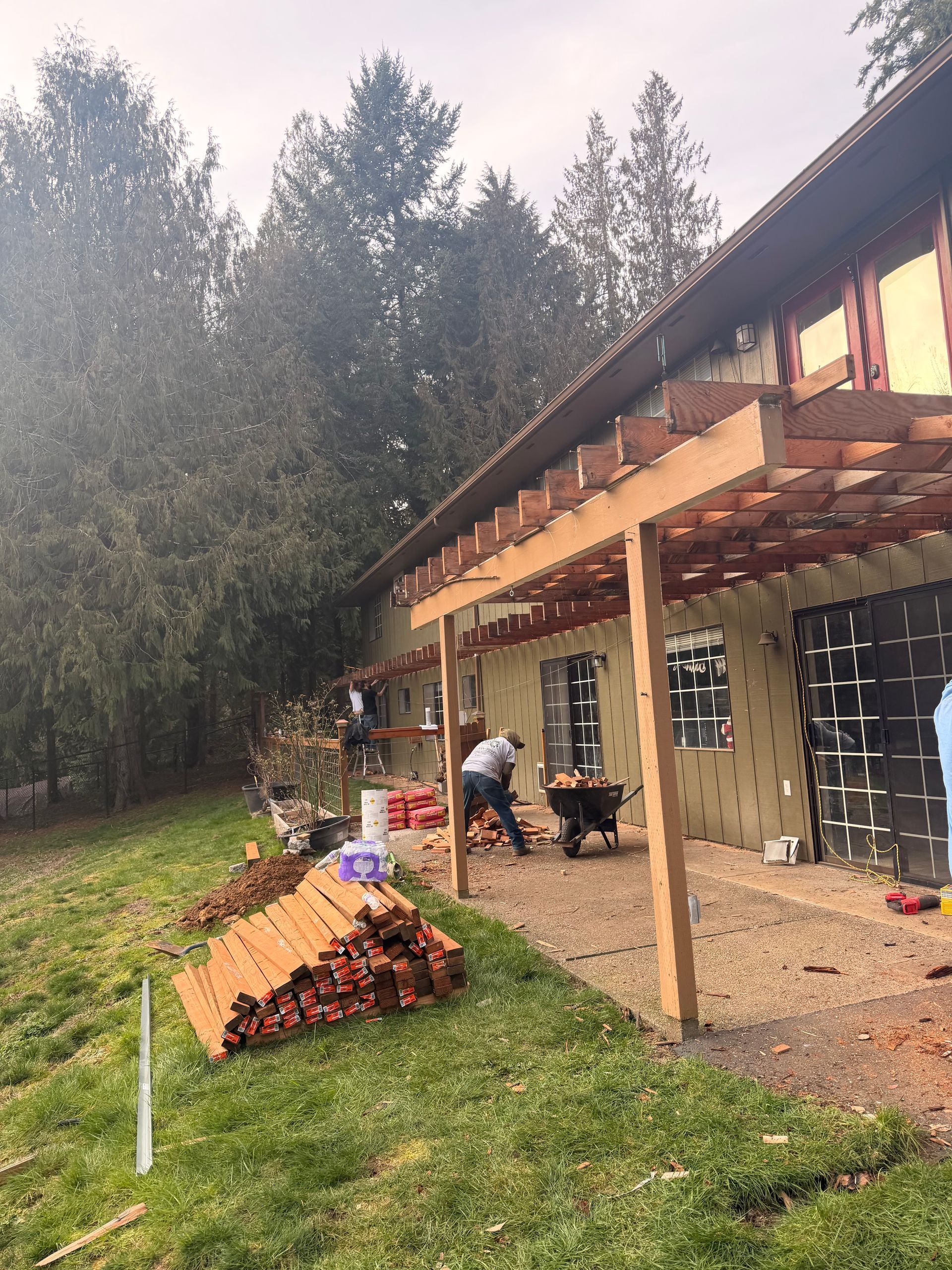 Rural porch under construction beside a grassy yard, with stacked red tiles and trees in the background