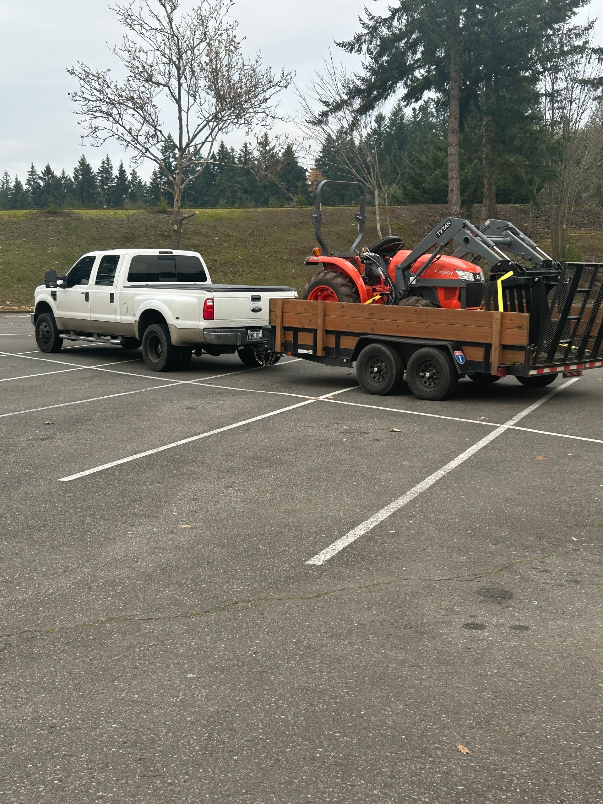 White pickup truck towing an orange trailer with equipment in a mostly empty parking lot.
