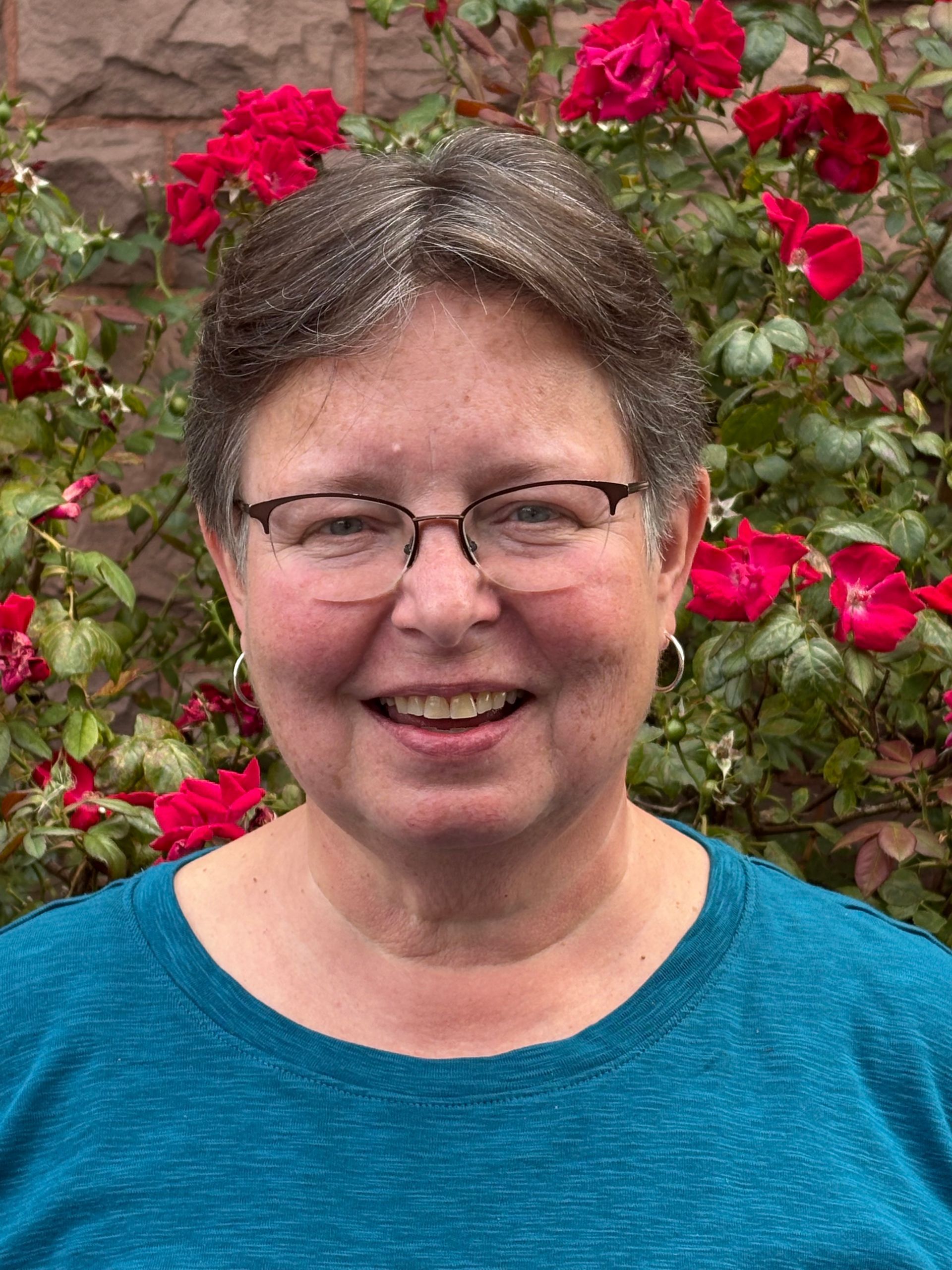 Smiling person in glasses and blue shirt in front of blooming red roses