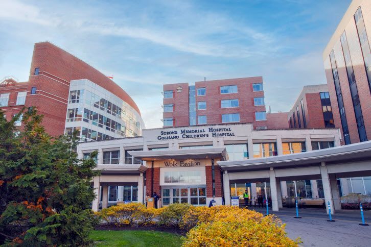 Exterior of a modern hospital entrance with red-brick buildings and a covered drop-off area