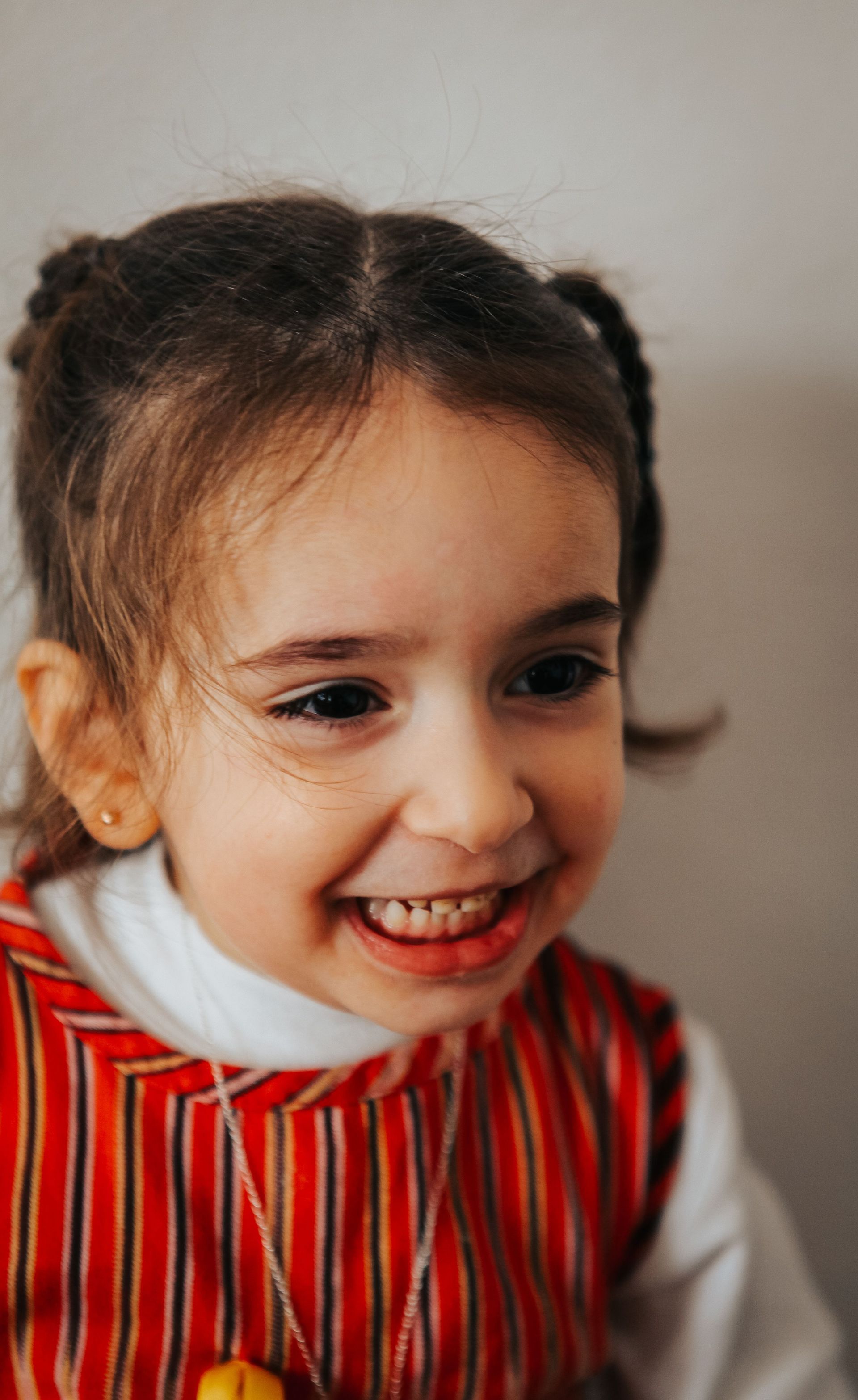Smiling child in a red striped shirt, looking to the side indoors.