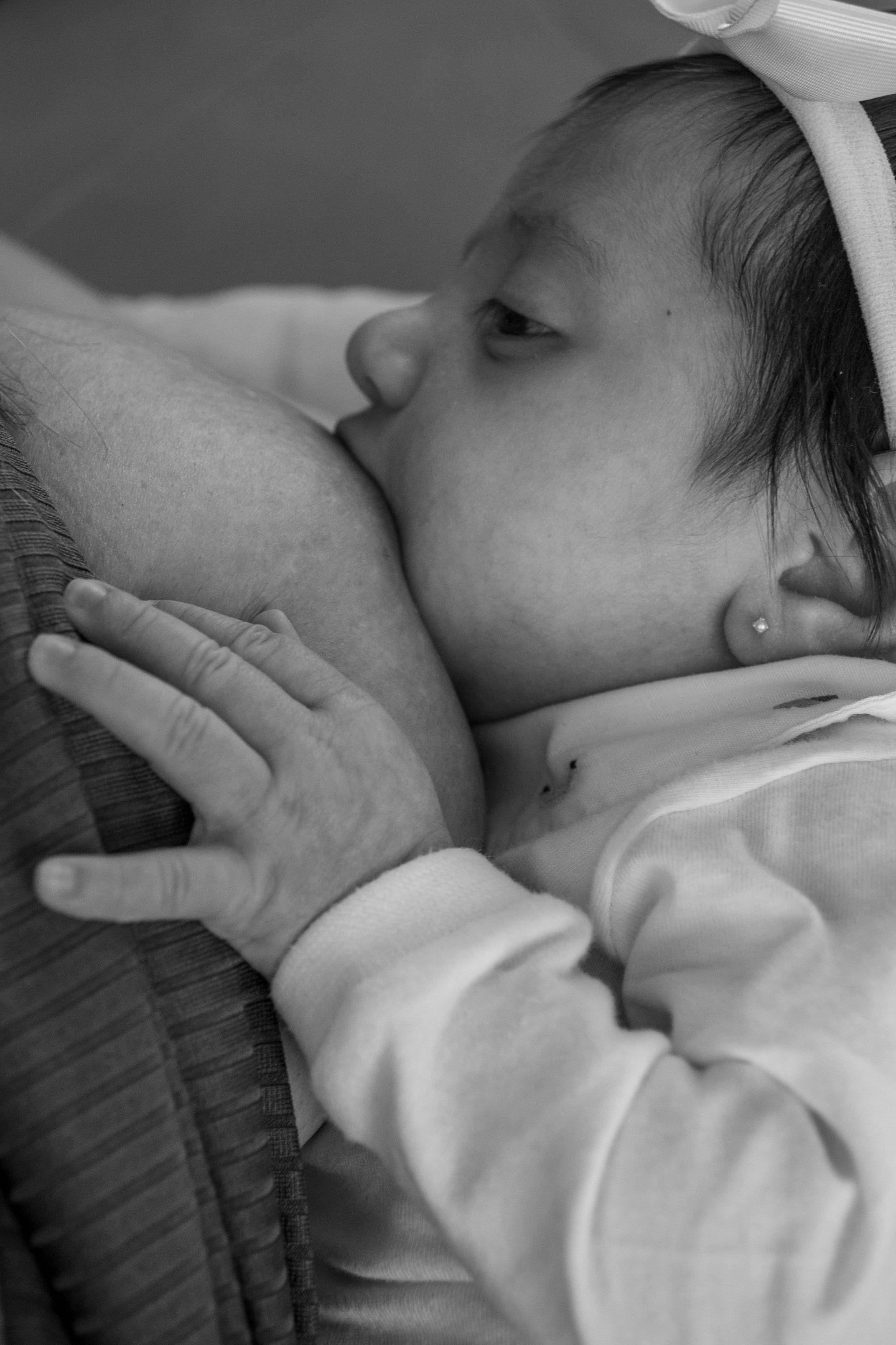 Baby nursing from a caregiver’s breast, in black-and-white close-up.