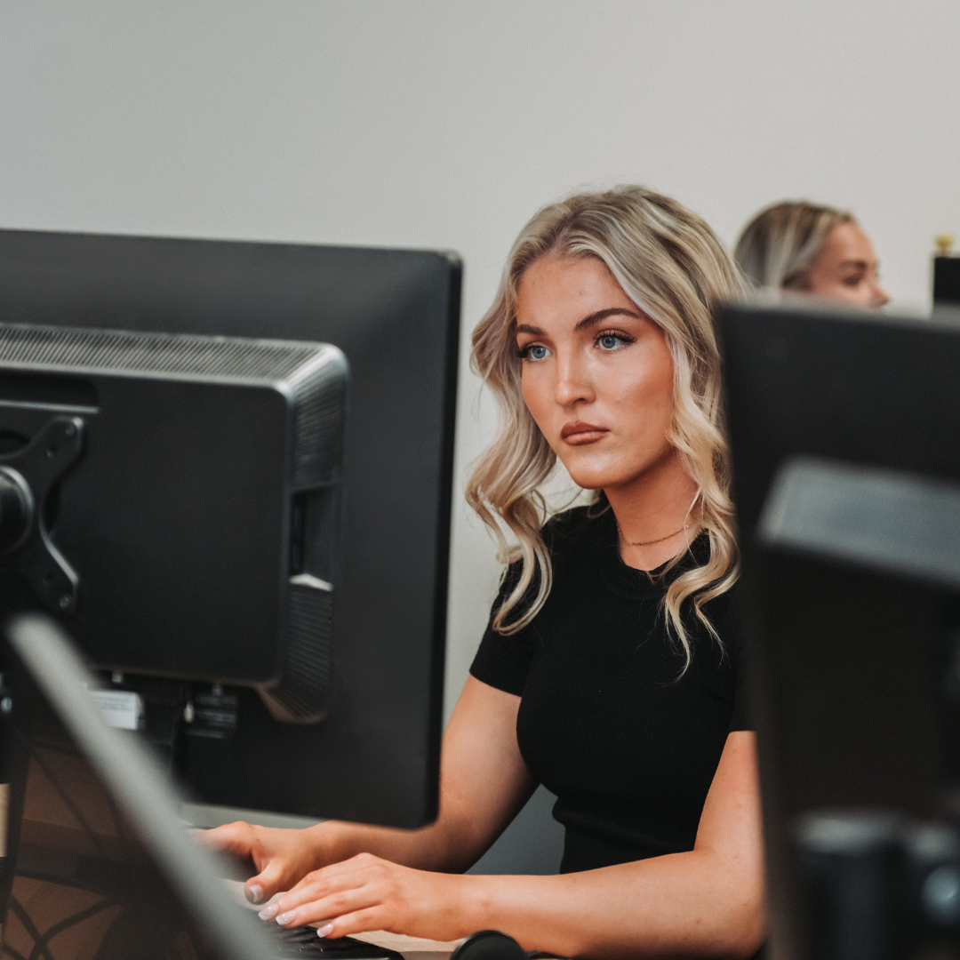 Woman typing at a desk with dual monitors in an office setting