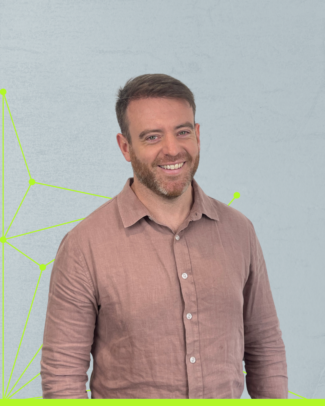 Smiling man in a pink button-up shirt standing against a light gray wall