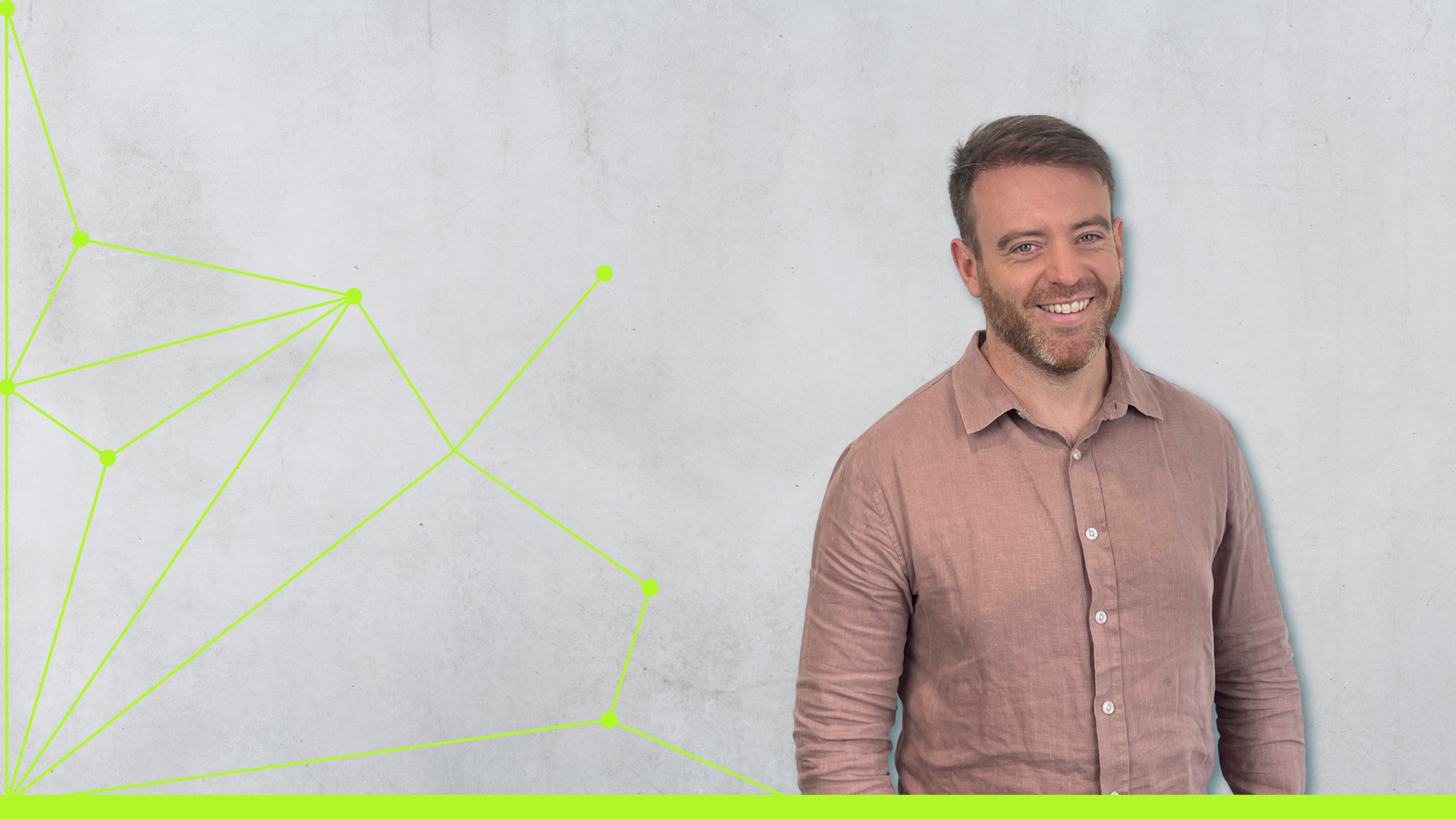 Smiling man in a pink shirt standing against a light gray wall with neon geometric lines on the left