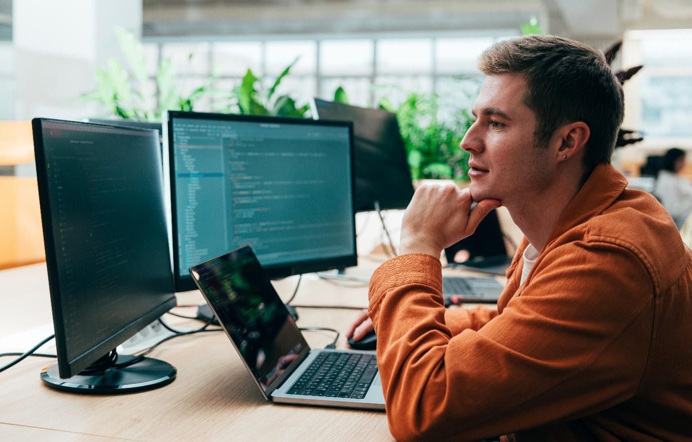 Person working at a desk with multiple monitors and a laptop in a bright office