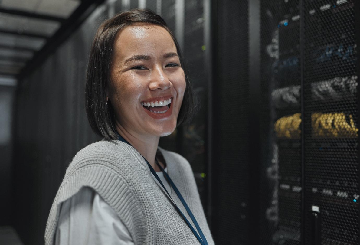 Smiling woman standing in a server room beside rows of computer racks