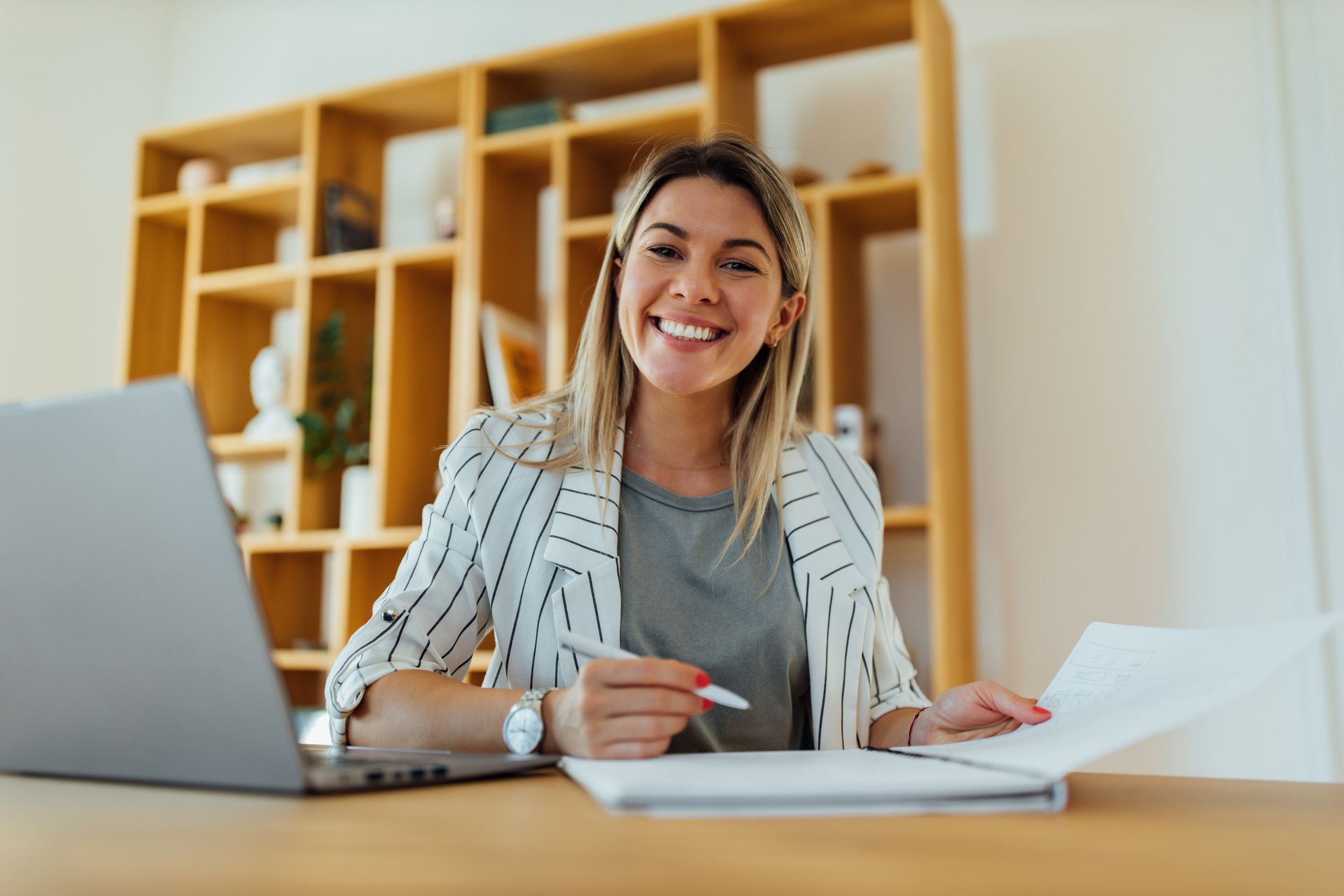Smiling woman at a desk with laptop and papers in a bright office