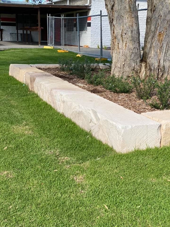 Retaining Wall Bordering A Garden Bed With Plants and Tree On A Grassy Area — Port Landscape Supplies in Port Macquarie, NSW