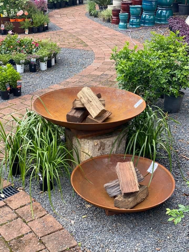 Two Rusty Metal Fire Pits with Firewood, on A Brick Path in A Garden — Port Landscape Supplies in Port Macquarie, NSW