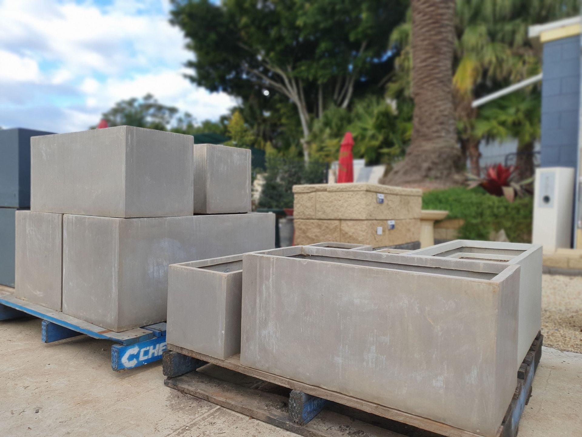 Concrete Planters Of Various Sizes Stacked On Pallets Outdoors — Port Landscape Supplies in Bonny Hills, NSW