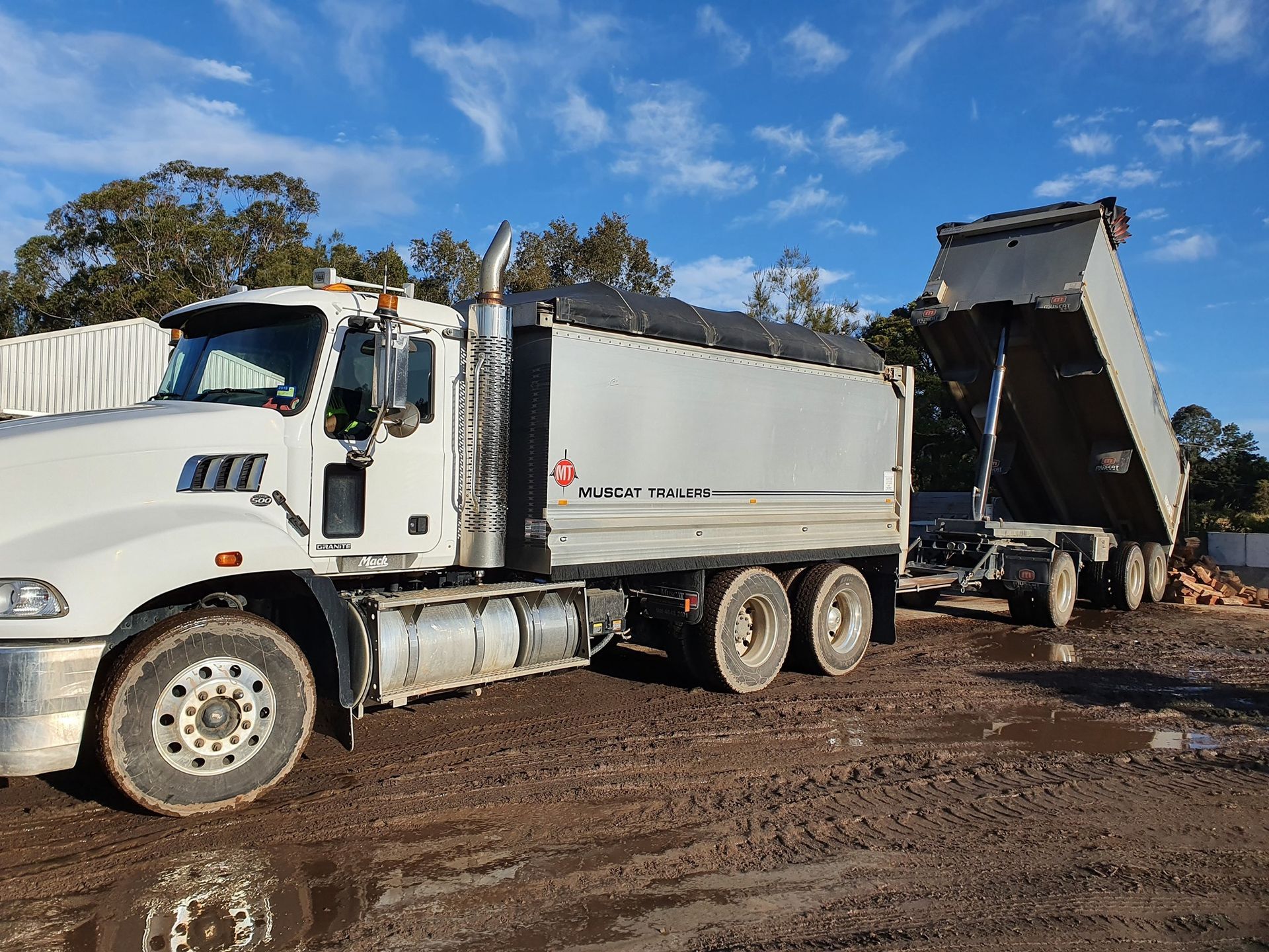 A White Dump Truck with A Raised Bed, Dumping a Load on A Muddy Surface — Port Landscape Supplies in Port Macquarie, NSW