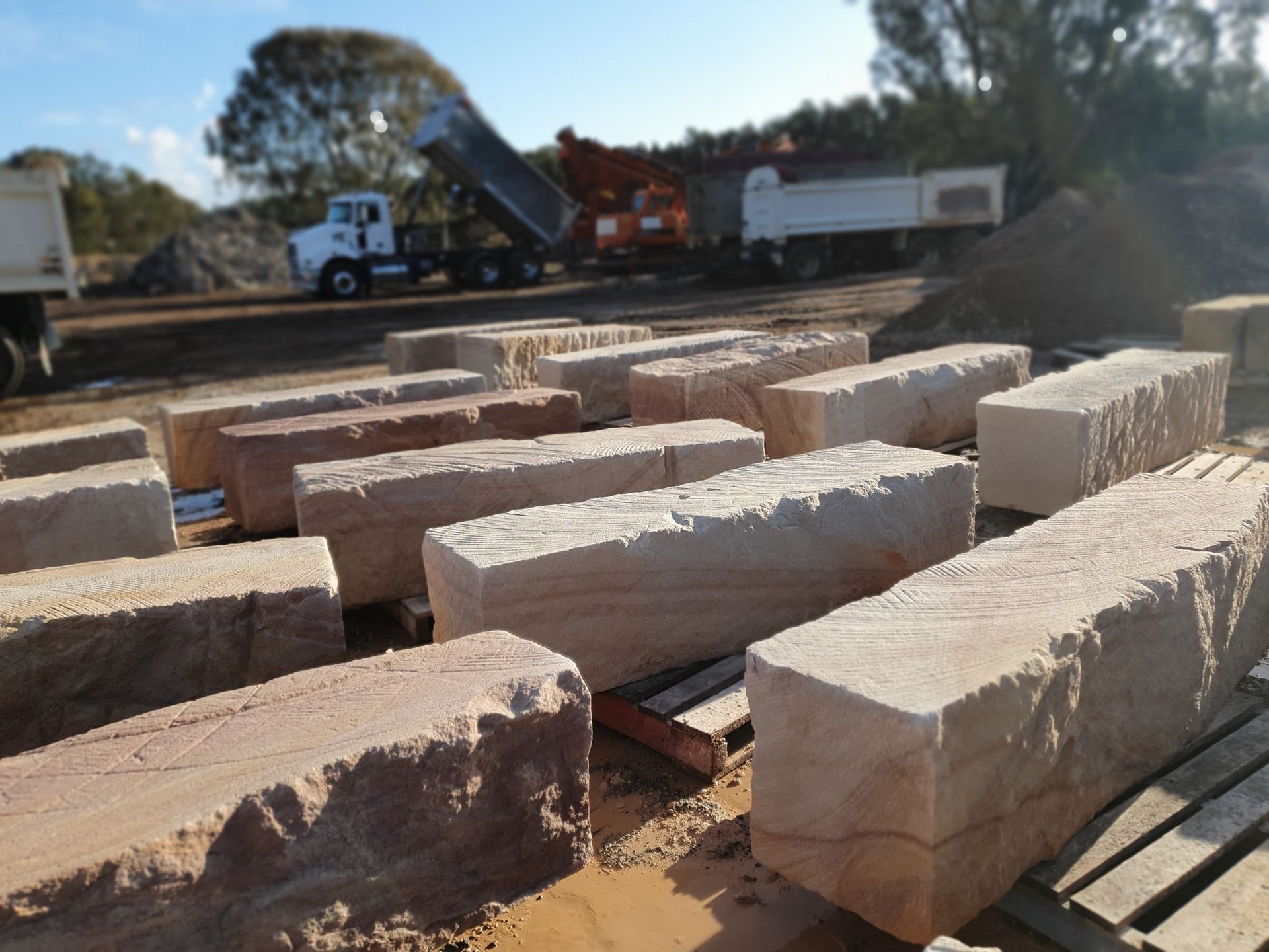 Rows Of Sandstone Blocks With Dump Trucks In The Background — Port Landscape Supplies in Port Macquarie, NSW