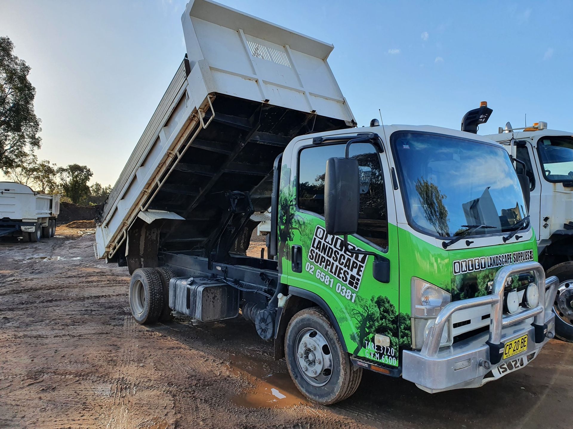 A White Dump Truck with Its Bed Raised, Parked Outdoors on Dirt — Port Landscape Supplies in Port Macquarie, NSW