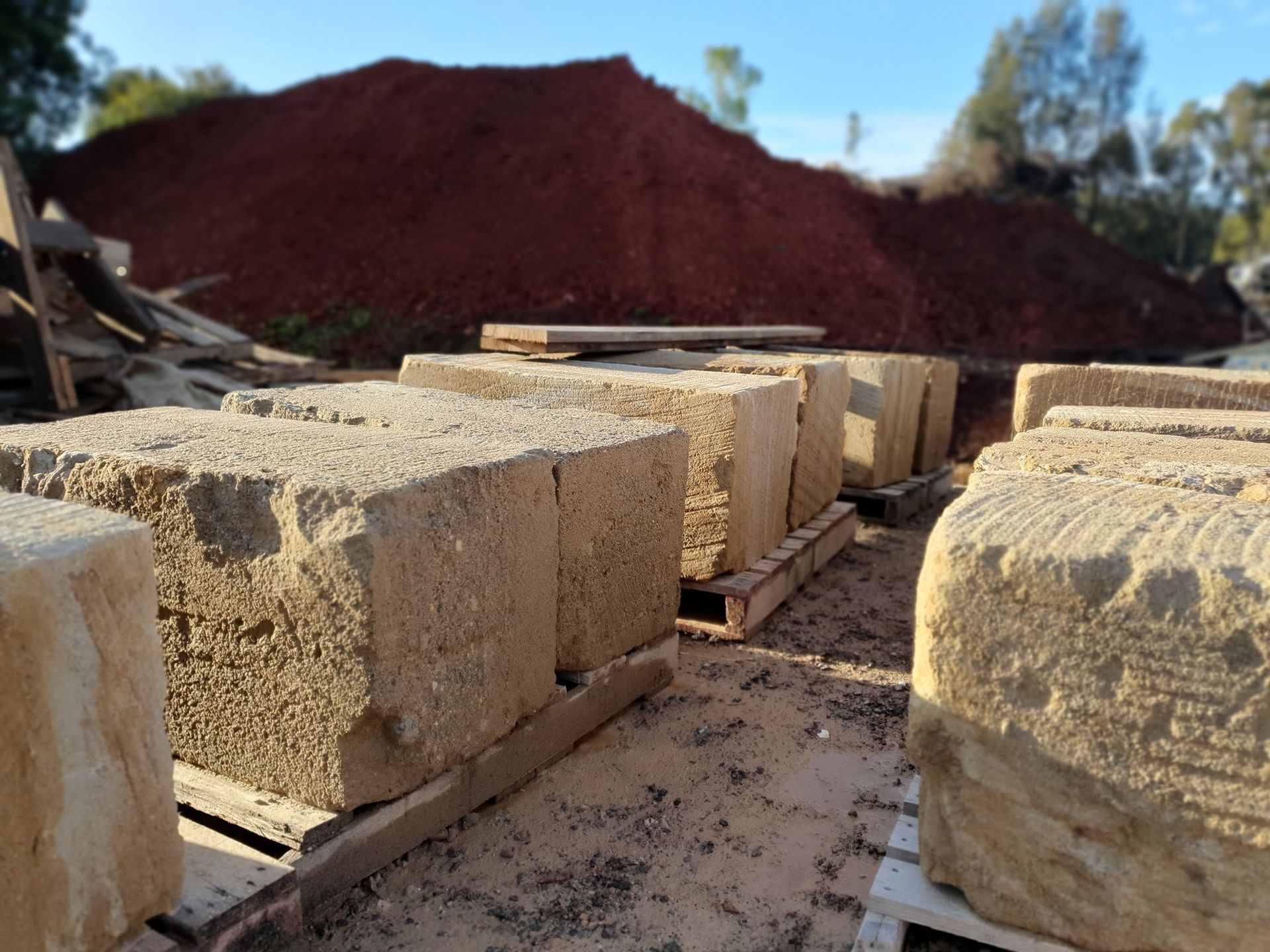 Stone Blocks Stacked On Pallets With A Large Pile Of Reddish Soil — Port Landscape Supplies in Port Macquarie, NSW
